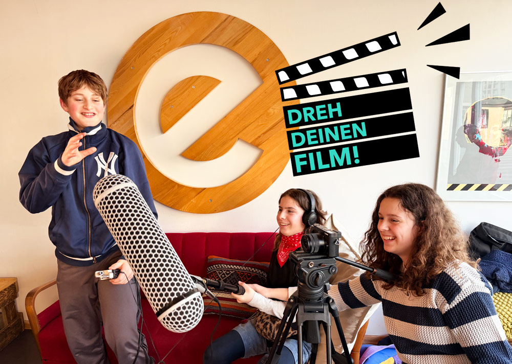 Jugendliche von DREH DEINEN FILM! e.V. haben auf der Couch im Esche Jugendkunsthaus eine Filmklappe und Mikrofon in der Hand.