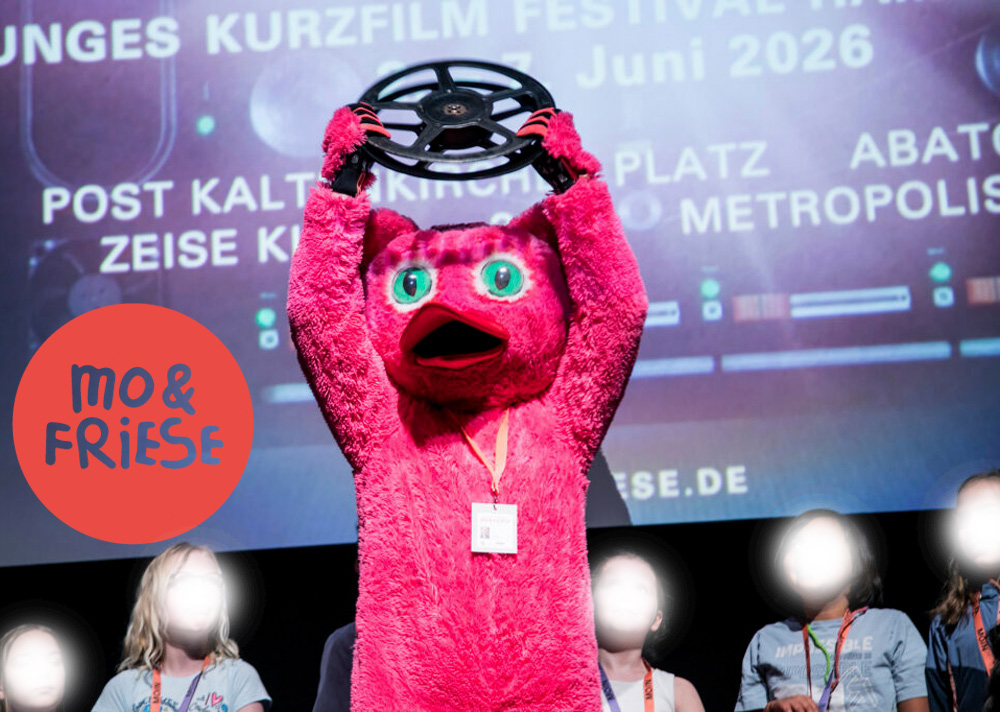 Auf der Bühne steht das rosa Plüschmaskottchen und hält eine Filrolle hoch, rundum Kinder.