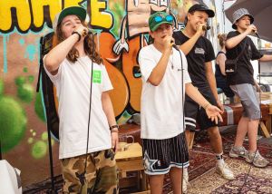 Vier junge Rapper performen mit Mikros in der Hand einen Song.